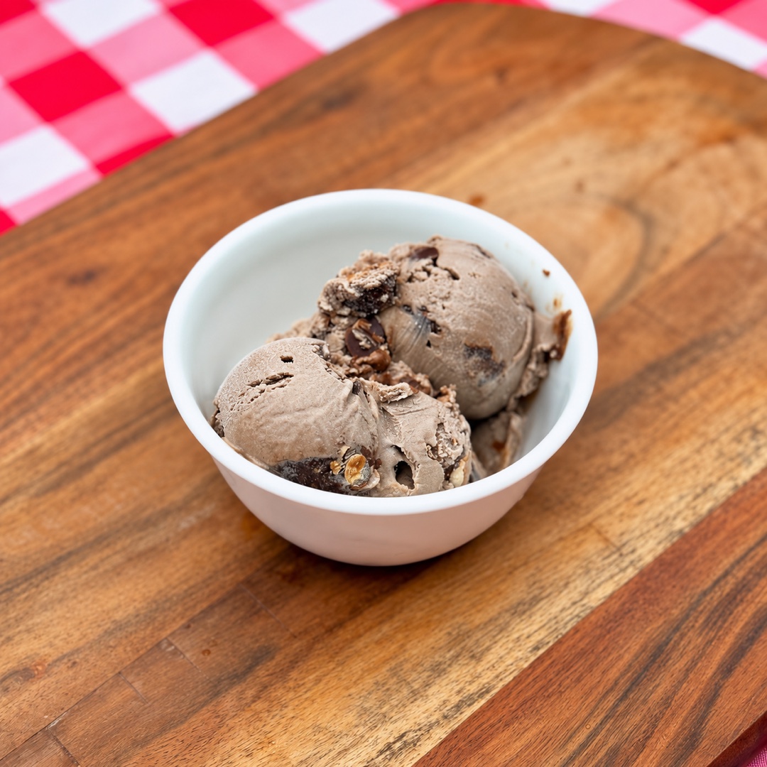 Cow Tracks Ice Cream wo scoops of Cow Tracks ice cream in a white bowl on a wooden board.